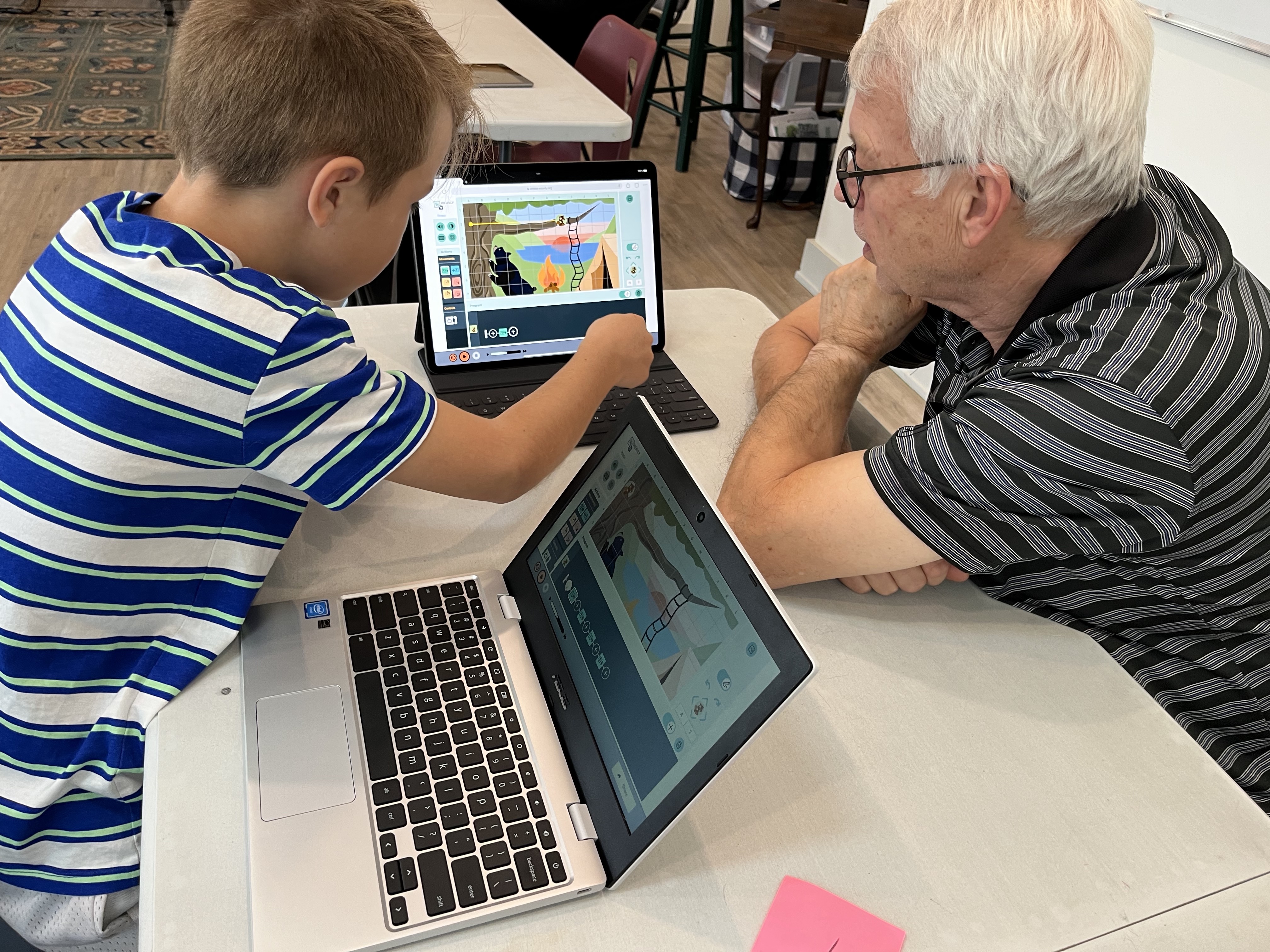 Young student showing an adult how to use Weavly coding environment on a laptop.